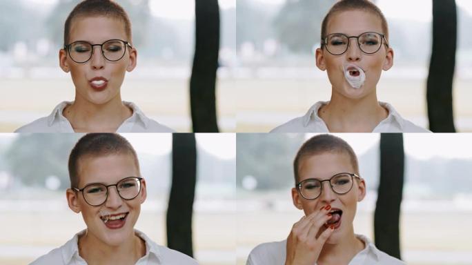 戴眼镜的迷人年轻女子咀嚼和吹泡泡糖