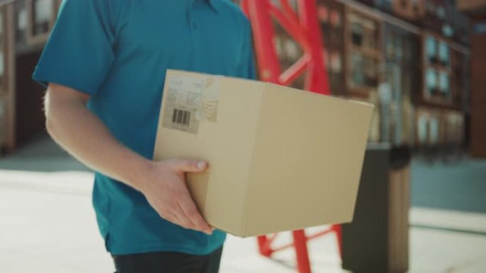 送货员拿着纸箱包装走过现代时尚的商业区。快递员在将邮政包裹交付给客户的途中。关注套餐。低角度慢动作