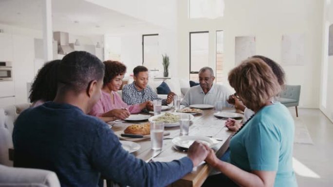 三代黑人家庭坐在餐桌上手牵手，饭前说恩典