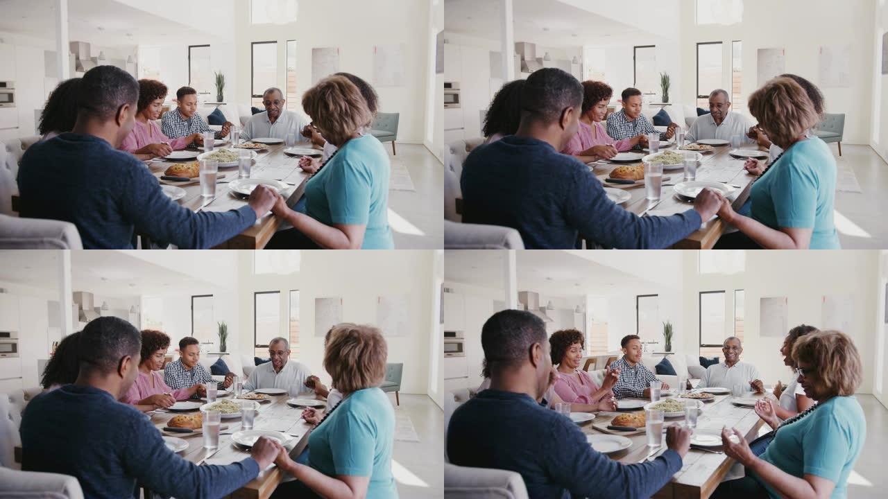三代黑人家庭坐在餐桌上手牵手，饭前说恩典