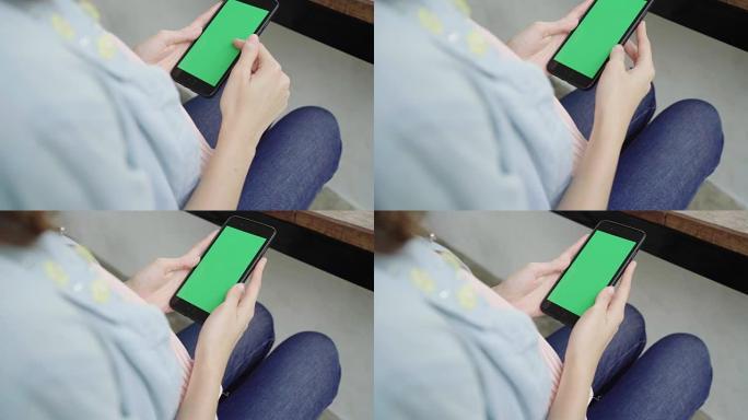 快乐快乐的亚洲年轻女子坐在咖啡馆里，使用带有绿屏的智能手机设备聊天、阅读和发短信。女性生活方式概念。