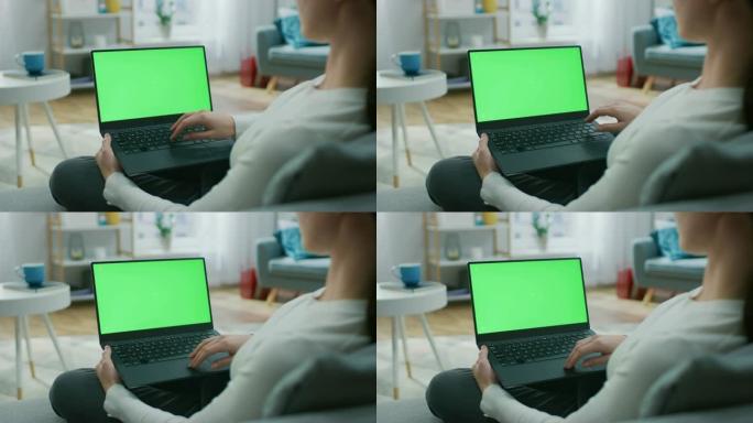 坐在沙发上的年轻女子在带有绿色模拟屏幕的笔记本电脑上工作。女孩使用电脑，浏览互联网，观看内容，与朋友