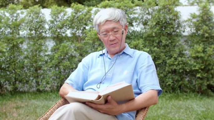 亚洲老人在家放松。亚洲高级中国男性享受休息时间戴眼镜看书，躺在花园里的早晨概念。