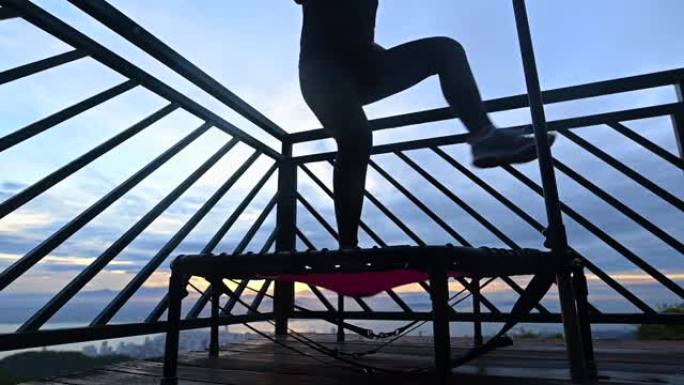 1名亚洲中国女运动员在槟城山日出时在蹦床上跳跃，有着戏剧性的天空和阳光