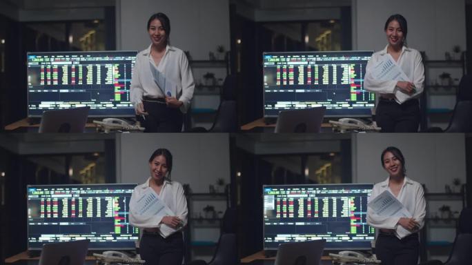 成功的美丽行政亚洲女商人的肖像智能休闲装看着相机和微笑，双臂交叉着电脑和证券交易所显示器在夜间办公室