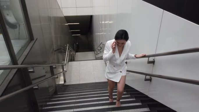 一名亚裔华裔年轻女白领从捷运站楼梯上走时通过电话交谈