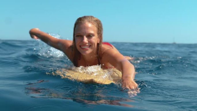 肖像: 微笑的冲浪女孩玩得开心，游泳到队伍里去捕捉波浪。