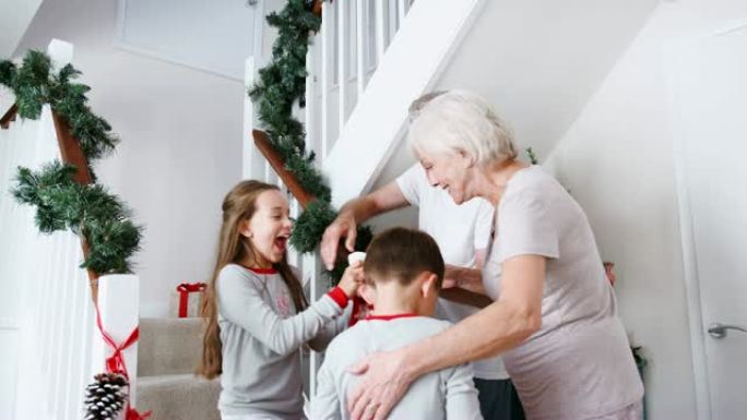 在圣诞节早上，祖父母向穿着睡衣的激动的孙子孙女打招呼，他们拿着袜子从楼梯上跑下来