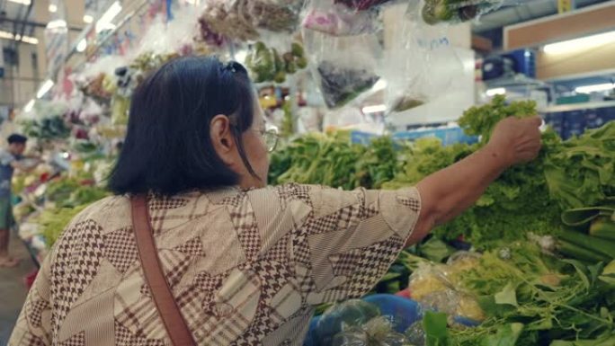 购买水果和蔬菜的亚洲高级妇女站在农贸市场