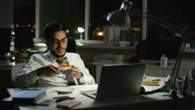 商人在黑暗的办公室吃披萨