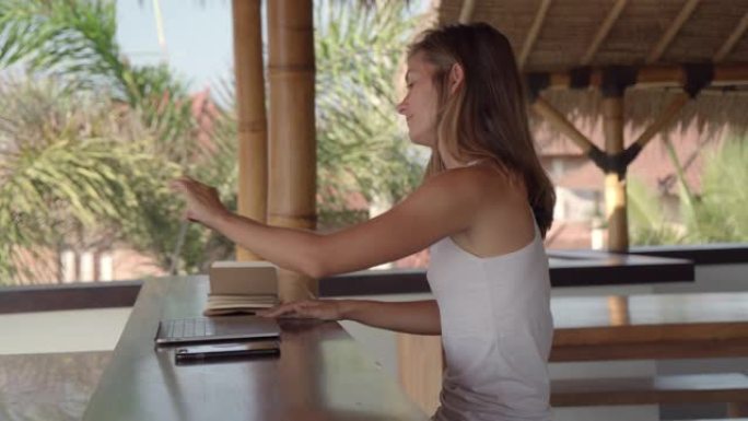 在茅草热带露台上使用笔记本电脑的女自由职业者