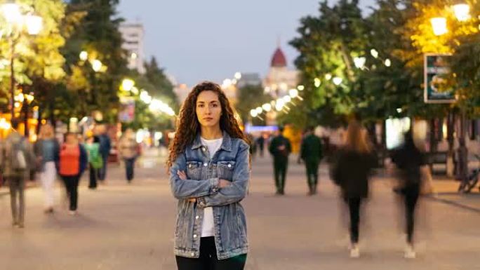 孤独的年轻女士站在市中心的街道上，双臂交叉，成群的男人和女人经过。孤独和时间概念。