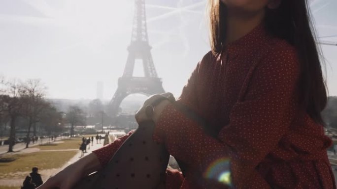 电影特写镜头，穿着红色连衣裙的美女坐在阳光明媚的埃菲尔铁塔上摆姿势，触摸双腿慢动作。