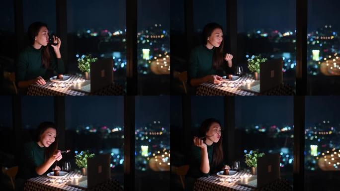 一位亚洲华裔美丽的年轻女士在魔术时刻，黄昏时在公寓里吃甜点，并使用笔记本电脑通过互联网与男友交谈