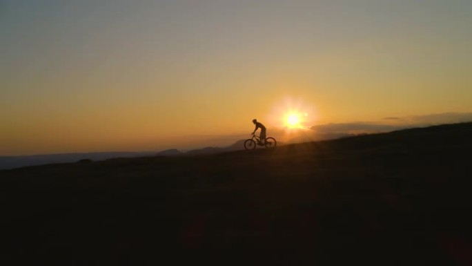 剪影: 无法辨认的人在日落时骑着山地自行车下坡。