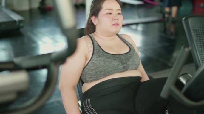 超重妇女在健身馆使用健身车进行有氧运动锻炼。