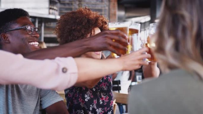 一群年轻朋友在餐厅酒吧见面时用啤酒敬酒-慢动作拍摄