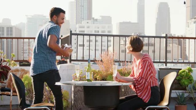 男人在屋顶露台上庆祝，以城市天际线为背景，给女人礼物