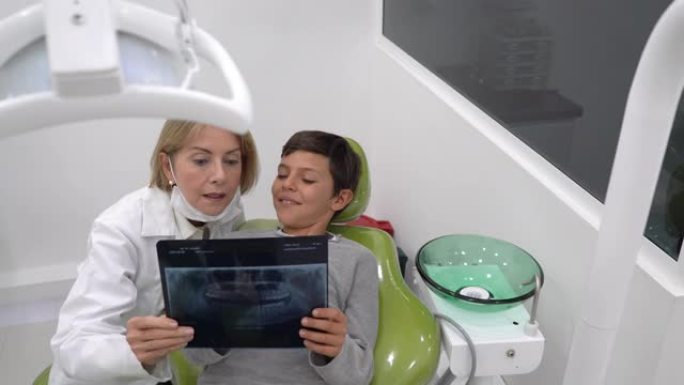女牙医向躺在牙医椅子上看x光的年轻患者解释一些事情