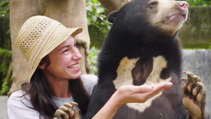 一个女人怀里抱着一只熊，给她喂食。