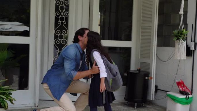 慈爱的爸爸把午餐盒交给女儿，并在离开学校之前在前廊亲吻她的再见