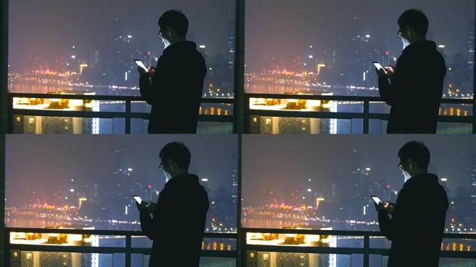 男人用手机和晚上夜深夜晚男人站在阳台玩手