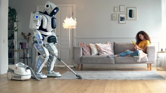 一个女孩躺在沙发上时，一个机器人做真空清洁。半机械人与人类概念。