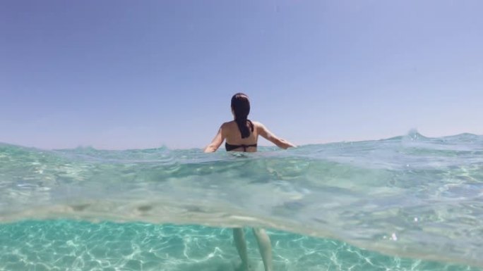 度假期间，年轻女子的慢动作在热带海水的透明蓝色海水中漂浮着腹部放松