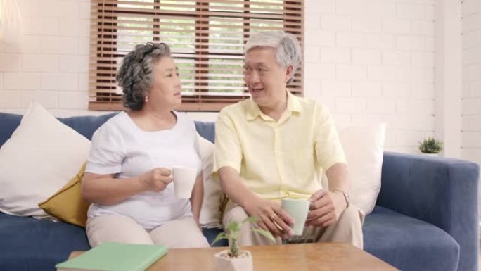亚洲老年夫妇在家里的客厅喝热咖啡，一起聊天，夫妇在家放松时躺在沙发上享受爱情时刻。生活方式高级家庭在