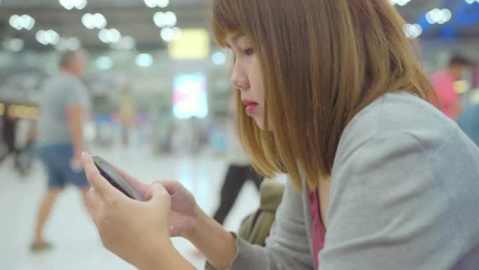亚洲妇女坐在国际机场时使用智能手机。