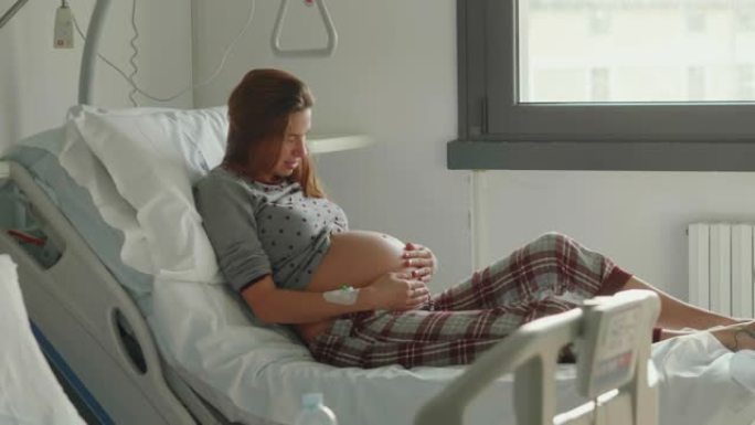 一名穿着睡衣的年轻孕妇的真实照片在医院分娩前几个小时抚摸着她的肚子