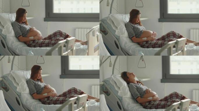 一名穿着睡衣的年轻孕妇的真实照片在医院分娩前几个小时抚摸着她的肚子