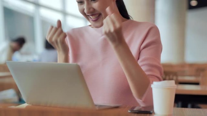 成功的亚洲女商人高兴地看着笔记本电脑兴奋地表达了胜利的姿态，举手是庆祝商业成功的胜利结果。成功，庆祝
