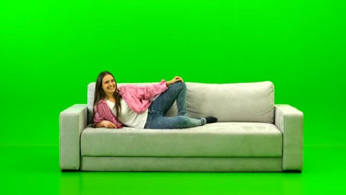 笑的女人躺在绿色背景上的沙发上
