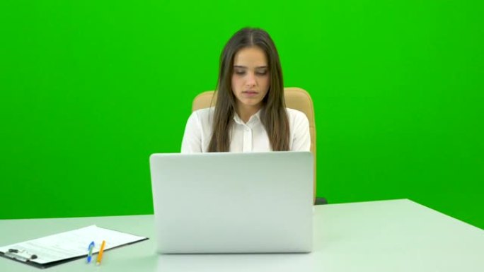 在绿色背景上的台式机上使用笔记本电脑的女人