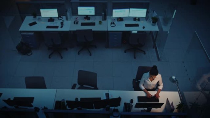 独自在办公室深夜工作: 女商人使用台式计算机，分析，使用文档，解决问题，完成项目。高架高角度射击