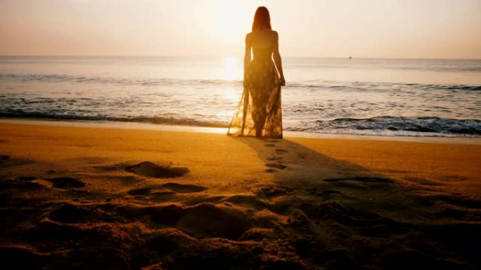 史诗般的背景照，年轻的幸福的女人穿着夏装走在令人惊叹的金色日落海洋海滩的水边。