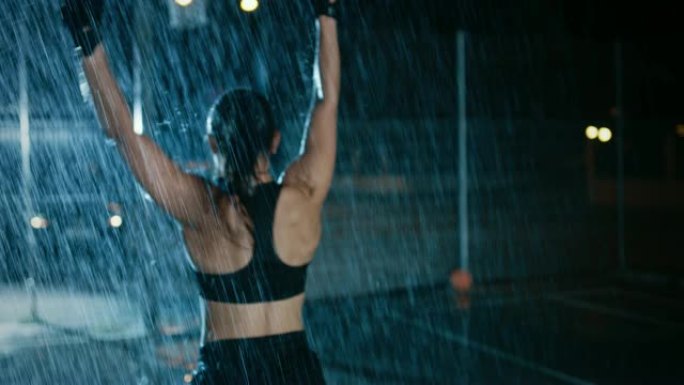 美丽的运动健身女孩正在庆祝她的运动成就。她晚上在大雨中欢呼，身后有一盏灯。