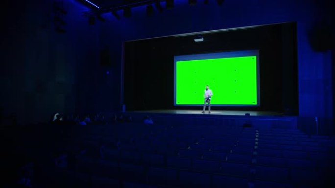 主旨发言人向观众展示新产品，在他身后的电影院配有绿屏、模型和色键。商务会议现场活动或设备展示