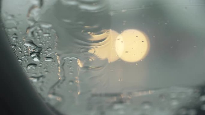 在雨中工作的汽车挡风玻璃雨刷。从挡风玻璃上可以看到过往汽车交通的模糊灯光。水沿着挡风玻璃流下。UHD