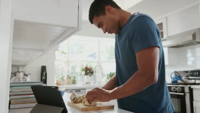 年轻的黑人男子使用平板电脑上的食谱在厨房里准备食物，特写，侧视图