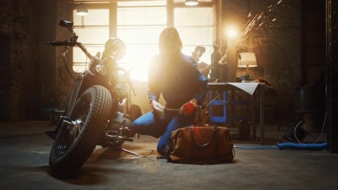 年轻漂亮的女机械师正在设计一辆定制的Bobber摩托车。穿着蓝色连体裤的天才女孩。她用棘轮扳手拧紧螺