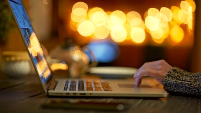女人穿着毛衣，喝了一口咖啡，通过笔记本电脑上网。明亮的黄色圆圈bokeh背景。滑动镜头，4K