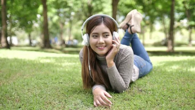 年轻女子少年躺在草地上的耳机上享受最喜欢的音乐