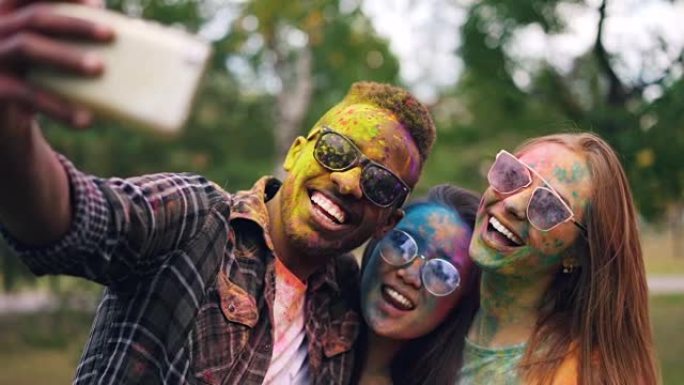 戴着墨镜的非裔美国人在Holi color holiday与女性朋友自拍，她们的脸和头发都被多色油漆