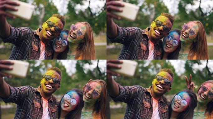 戴着墨镜的非裔美国人在Holi color holiday与女性朋友自拍，她们的脸和头发都被多色油漆