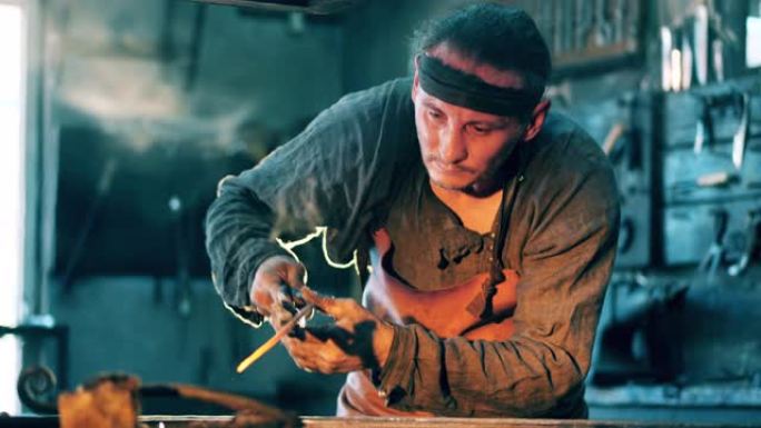 男子在锻造厂用刀工作时拿着金属钳。