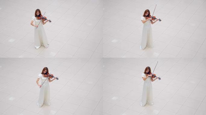 一个穿着白色连衣裙的女孩独自站在一个房间里拉小提琴。