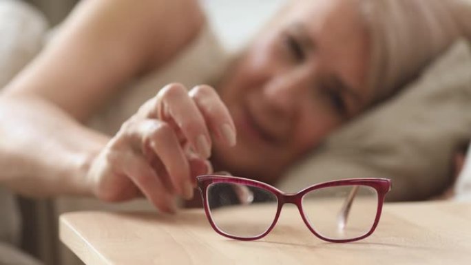 年长的成熟女人从床头柜上拿光学眼镜。