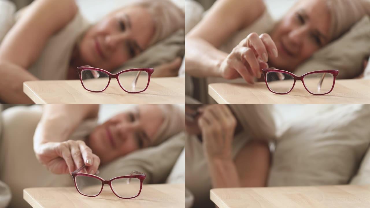 年长的成熟女人从床头柜上拿光学眼镜。
